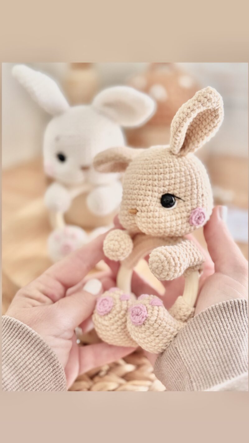 Handmade crochet bunny rattle with open arms – side view – beige and off-white version – held by designer’s hands