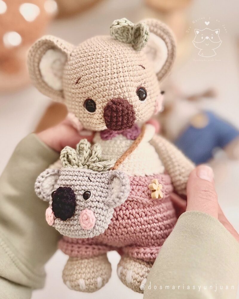 Close-up of Benna the crochet koala with a tiny koala backpack, handmade with pastel yarns. Designed by Dos Marías y un Juan.