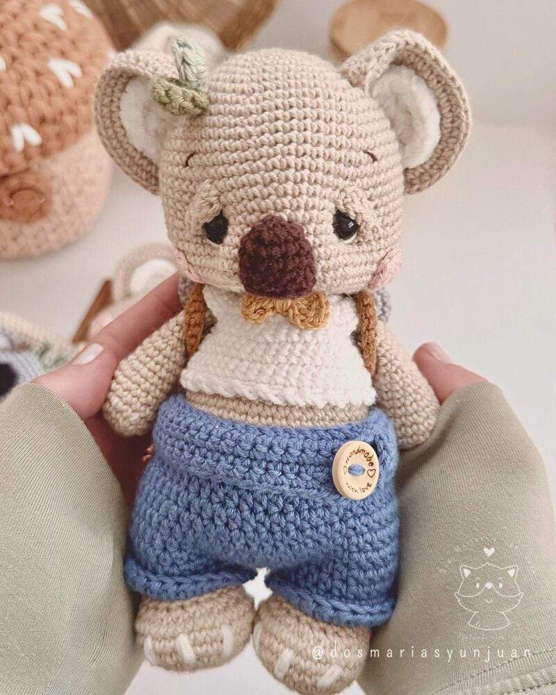 Benny the crochet koala doll wearing blue shorts and a bow tie, shown without backpack. Handcrafted toy designed by Dos Marías y un Juan.