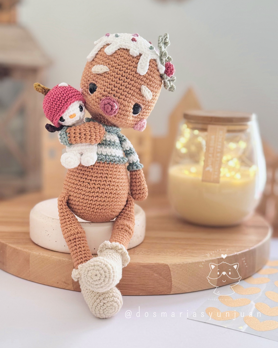 Candito gingerbread amigurumi sitting with Snowy Micro Snuggler, candle lights and wooden holiday decor.