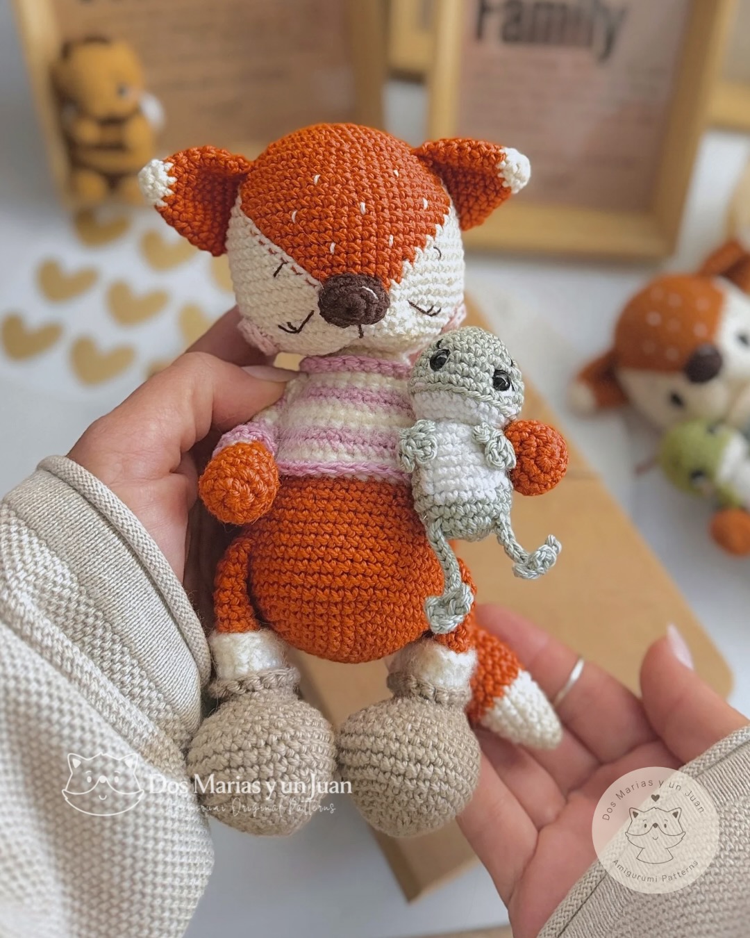 Two amigurumi Emilio the Fox variants side by side — awake face with René the Tree Frog and sleepy face with a mouse companion — handmade in crochet, styled with a wooden "Family" frame in the background.